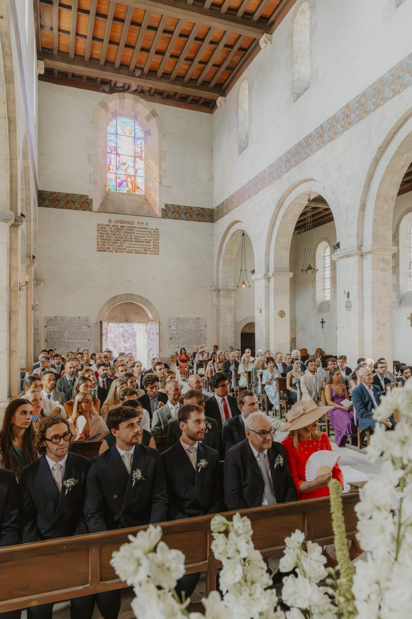 Les invités dans l’église lumineuse, sous le plafond de bois peint et le vitrail
