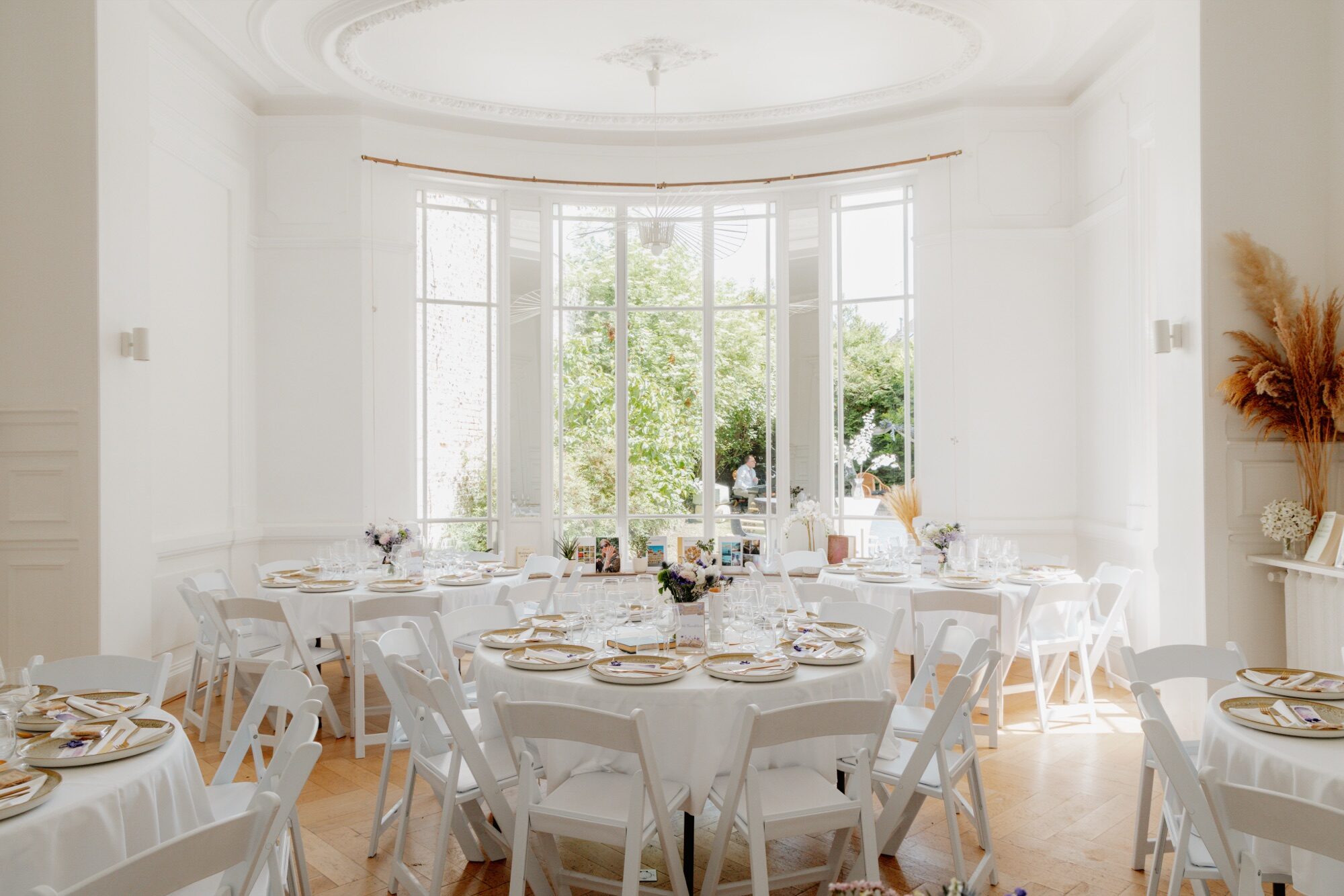 Salle de réception de l’Hôtel particulier 119 : rotonde vitrée ouverte sur le jardin, moulures, tables rondes nappées de blanc