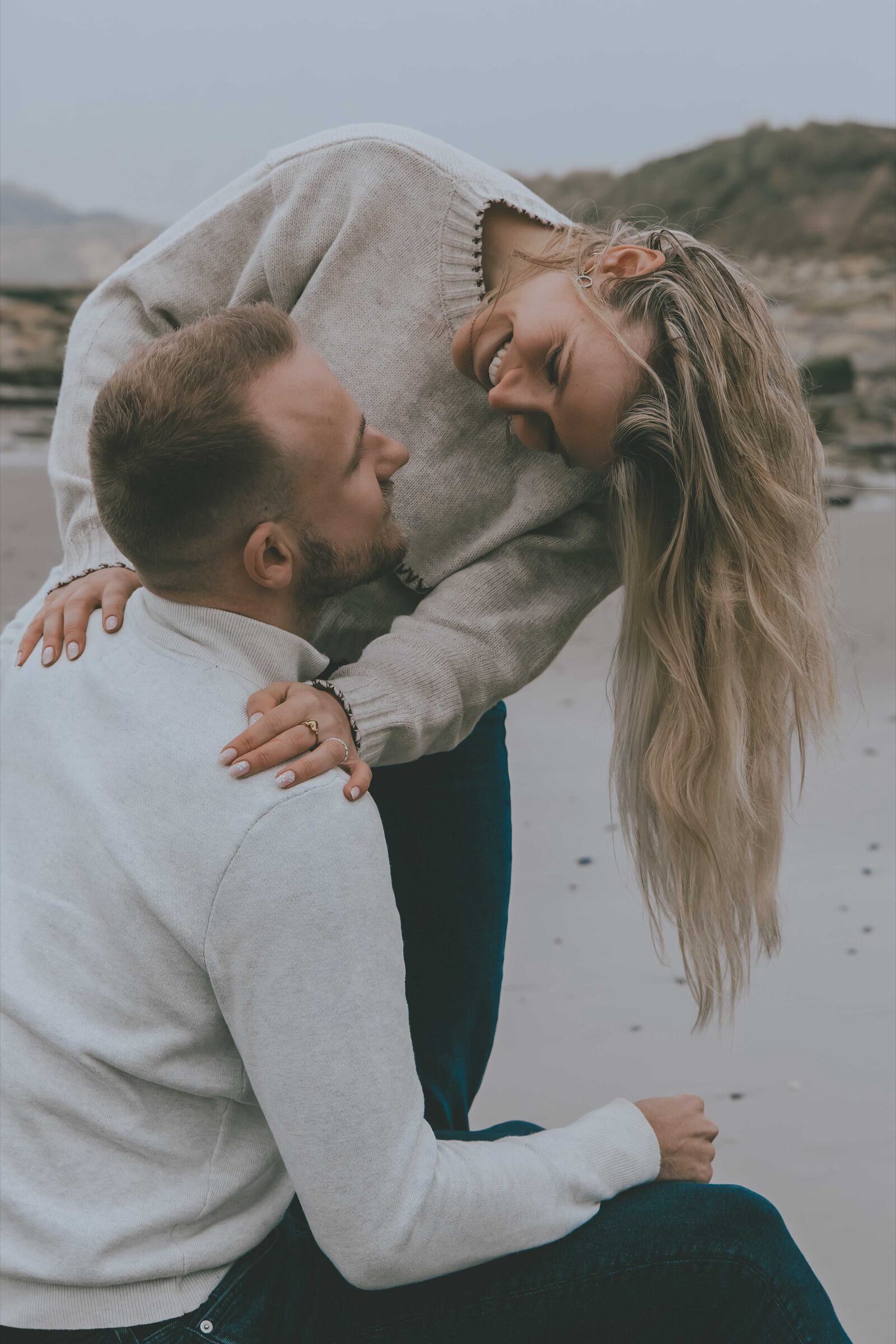 Elle se penche en riant sur lui, assis sur la plage — photo de couple Côte d’Opale