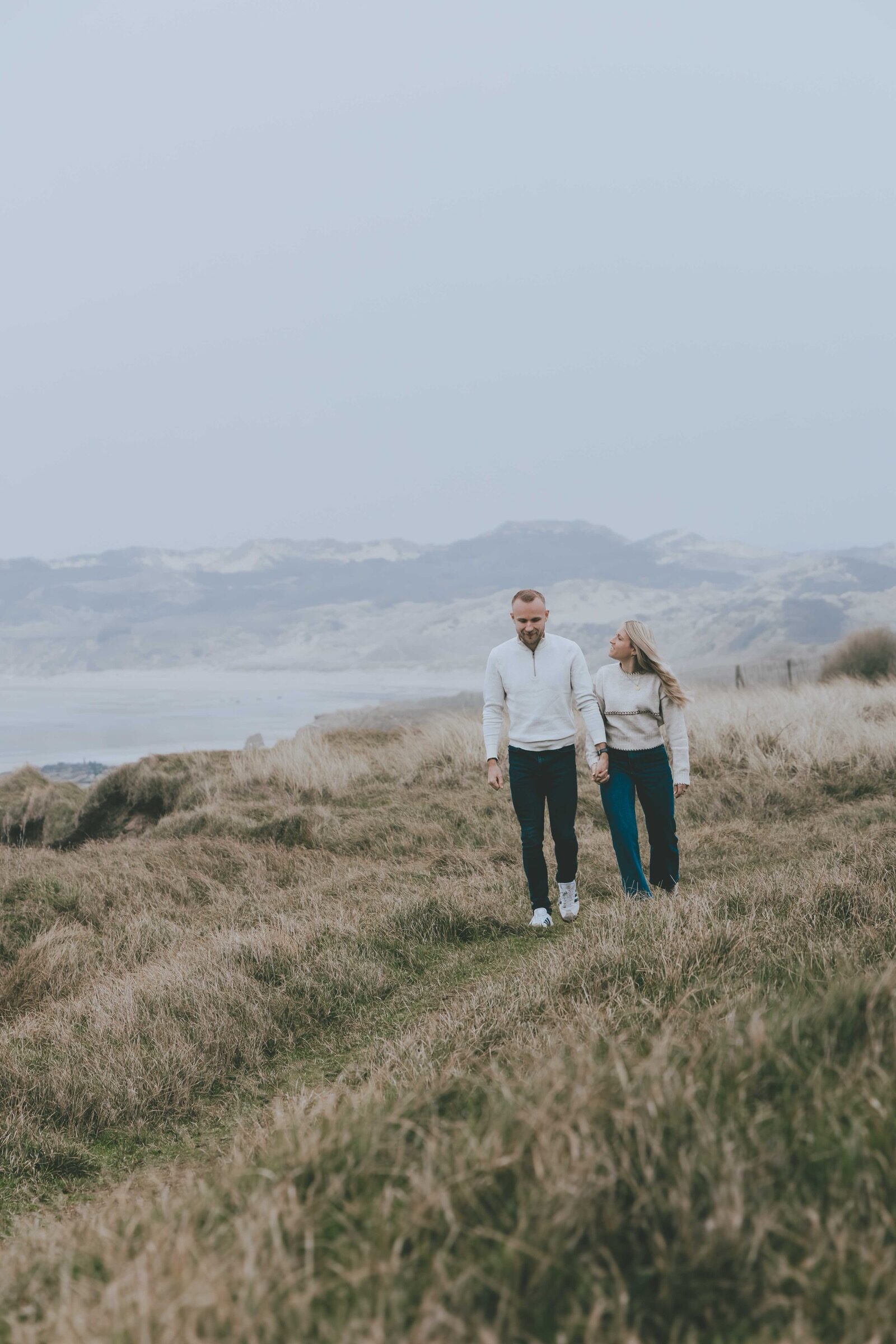 Couple main dans la main dans les dunes face à la mer — séance photo Côte d’Opale