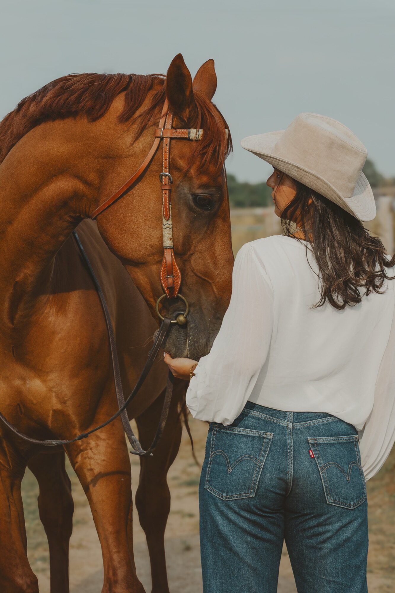 Cavalière au chapeau tenant son cheval alezan