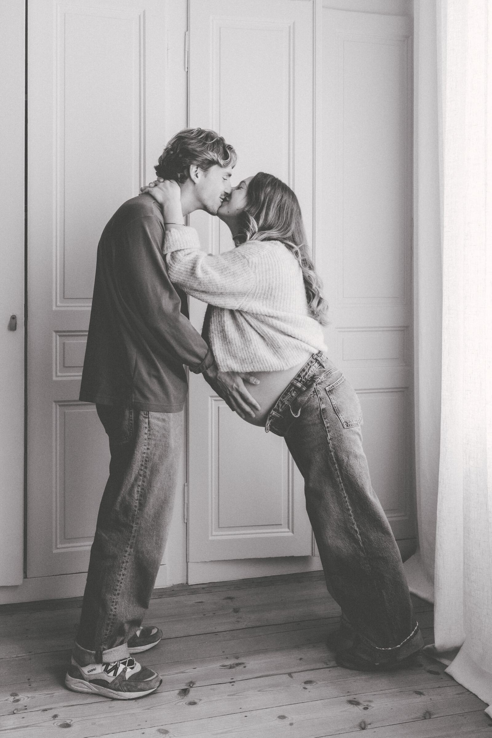 Futurs parents qui s’embrassent devant une porte, en noir et blanc — photo de grossesse