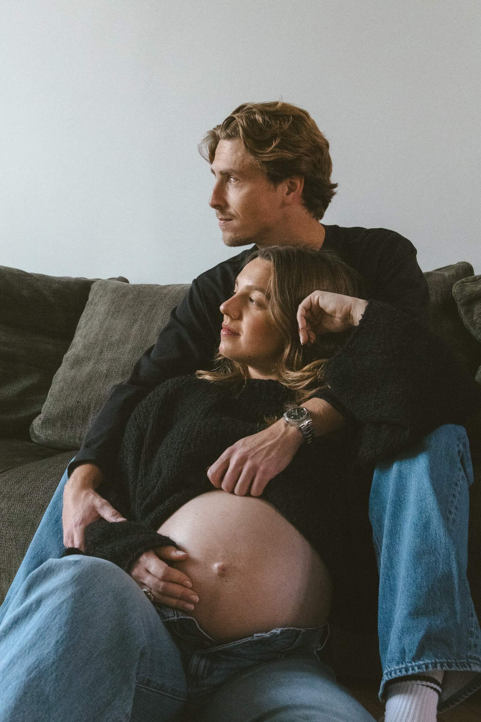 Future maman sur le canapé, futur papa qui regarde au loin — photo de grossesse à domicile