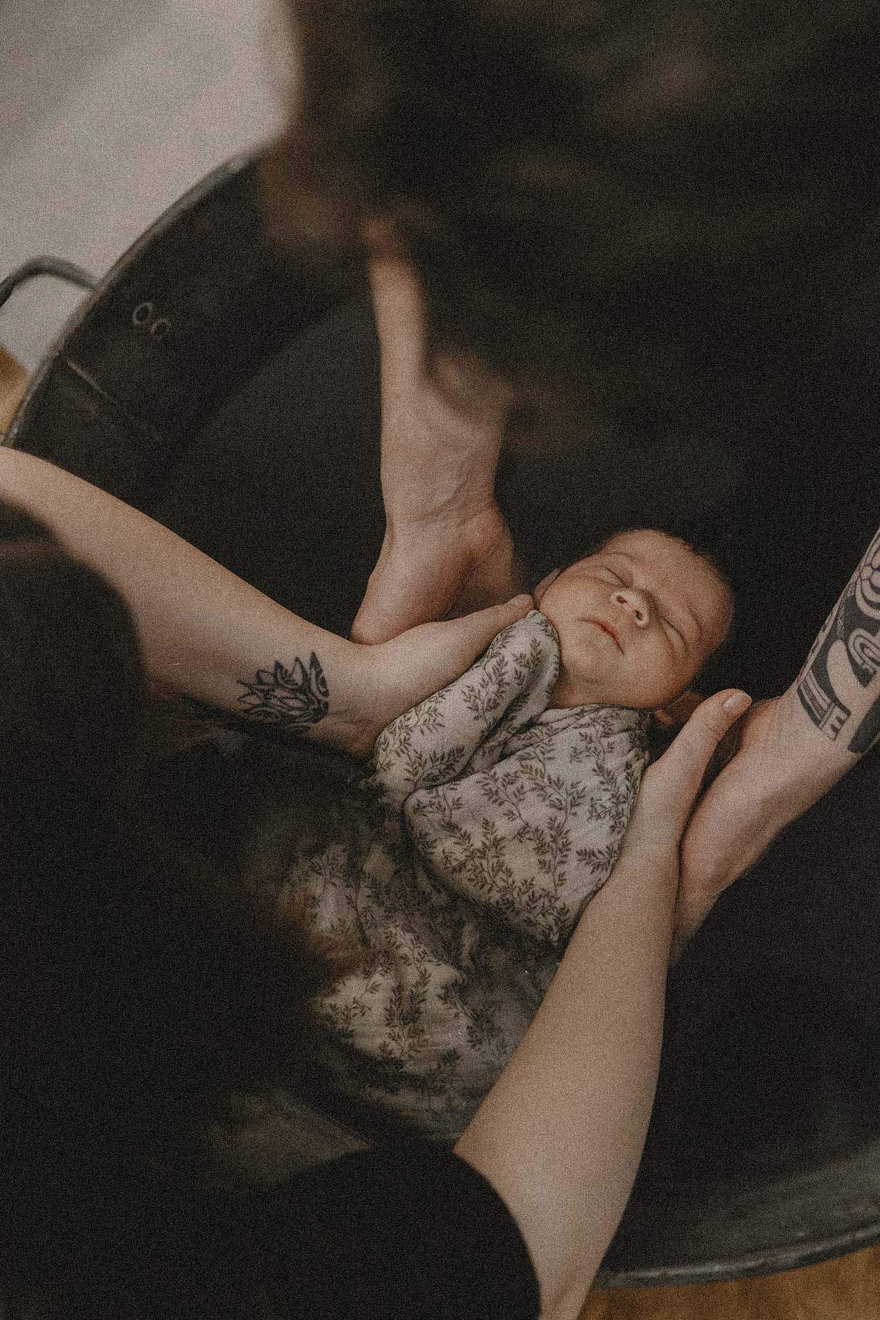 Bain de bébé tenu par des mains tatouées — séance photo de naissance à domicile
